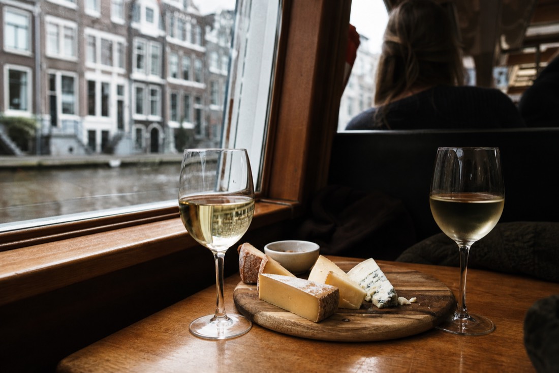 Cheese board and wine glasses on a wooden boat table with canal houses in the background, no text, no logos, no people