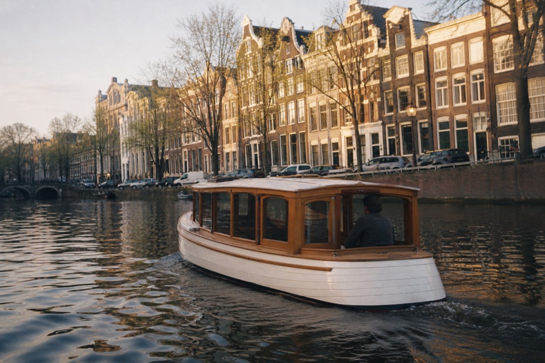 A classic saloon boat gliding along the Herengracht at golden hour, gabled canal houses reflected in the water, no text, no logos, no people