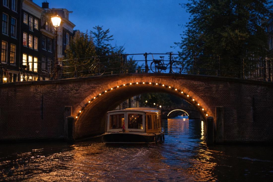 A canal boat passing under a lit stone bridge at dusk in Amsterdam, no text, no logos, no people