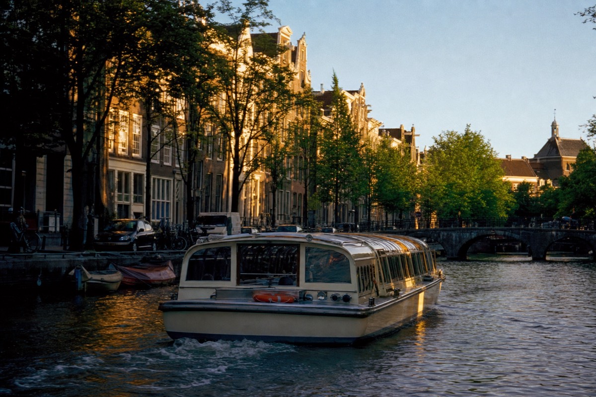 A saloon boat gliding along the Prinsengracht in warm late afternoon light, no text, no logos, no people.