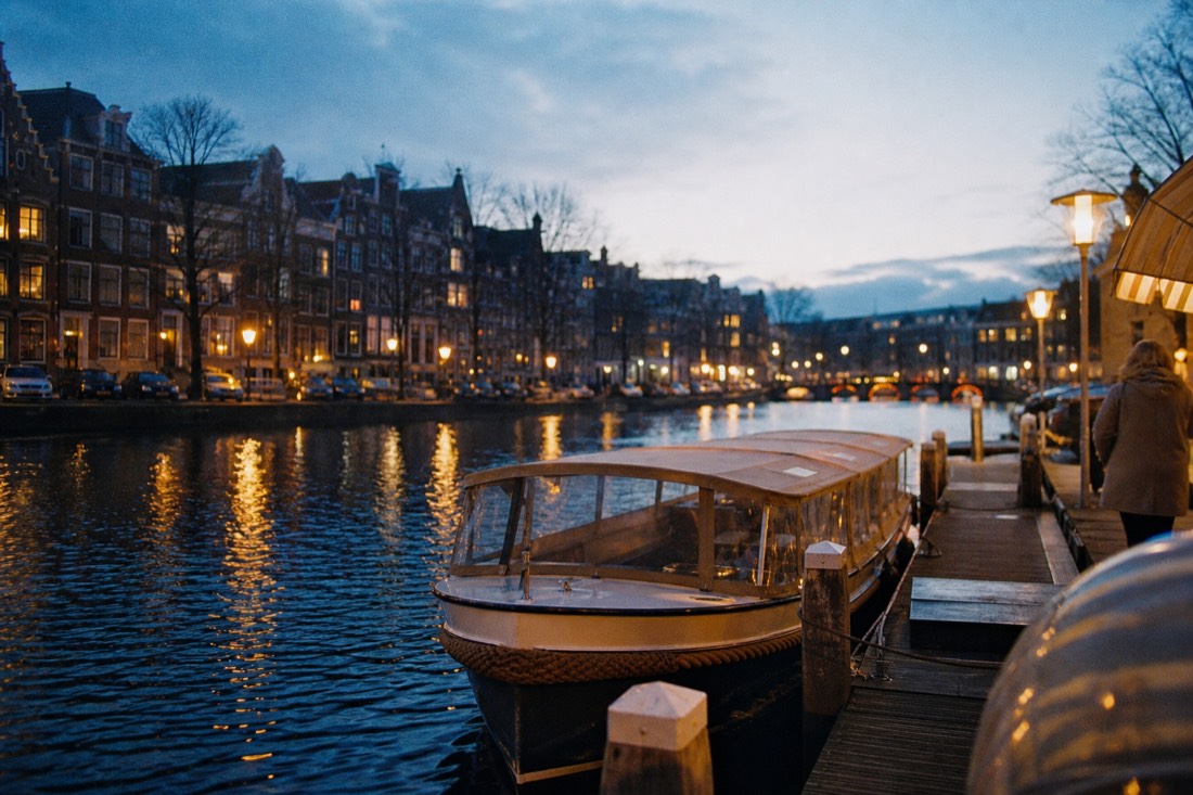 A jetty on the Prinsengracht with a small covered saloon boat tied up at dusk, no text, no logos, no people